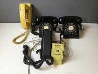 Four vintage phones arranged with two black rotary dial phones, one black push-button phone and one yellow wall phone on neutral backdrop.