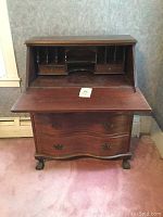 Full view of open secretary desk showing drop front writing surface, internal cubbyholes and drawers, serpentine front lower drawers, and claw feet.