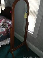 Front view of the full-length cheval mirror beside a bed, showing wooden frame and acrylic mirror surface