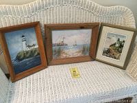 Three framed artworks displayed on a white woven couch, showing coastal scenes with lighthouses and ships.