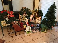 Wide view of Christmas decorations including artificial tree, wreaths, red sleigh with figures, gift boxes, and other assorted holiday items.