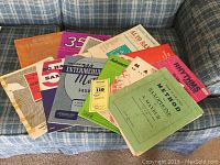 Full collection of alto saxophone instructional books laid out on couch showing variety of titles and colors.