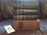 Three stacked volumes of the reproduction Encyclopedia Britannica with black and gold spine labels, sitting on top of a decorative box, plus a small tag.