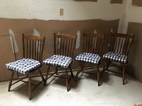 Four wooden Windsor chairs in a storage area, each with a blue and white checkered seat cushion, showing general condition and style.