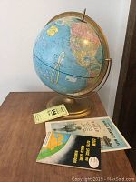 Photo of the vintage Cram's Sphere-O-Sphere 12-inch world globe on a gold-colored metal base with two accompanying booklets placed in front.