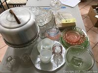 Top-down view of lot including pink and green depression glass bowls, white milk glass cups and saucers, aluminum covered cake saver, and clear textured glass bowls