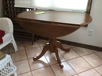 Round wooden drop leaf table with one leaf extended seen from side angle showing the extension and pedestal base with curved legs.