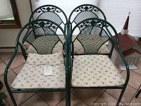 Four green metal patio chairs with lattice backs and floral cushions arranged indoors on tiled floor.