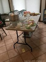 Folding table set up with various dishes and glassware on top, showing the table surface and overall size.
