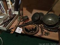 Photo showing a selection of brass and copper kitchen and decorative items including a decorative plate, wooden salad tongs, spice rack, and metal bowls.
