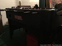 Side view of the black foosball table with 'REBEL' branding in a dimly lit room.