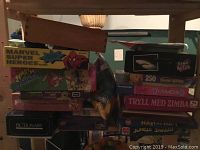 Two images showing stacked assorted board games including Marvel Super Heroes, Risk, Pictionary, Jumping Monkey, Hatt over Hatt Jungle Safari, Diamond, Tryll Med Zimba, a 250 piece Snow White puzzle, and True or False.