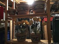 Five matching stone planters displayed on shelving with artificial yellow tulip flowers inserted in three of them.