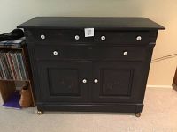 Front view of dark stained solid wood cabinet with three drawers and two doors showing white pulls and visible wear marks.