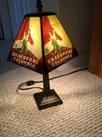 Lamp showing vintage Grafoni Columbia design on shade illuminated by lamp's light, base on carpeted floor.