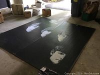 Two large black panels laid flat showing painted grayscale faces of The Beatles' band members. Panels have some wear and appear to be hand painted.