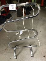 Curved metal Warmrails towel heater with power cord laid over the unit, showing chrome finish and minor surface wear
