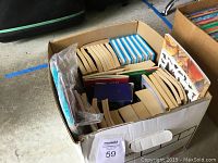Top-down photo of cardboard box filled with a mix of paperback and hardcover books, displaying various colorful spines and covers.