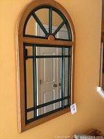 Front view of framed mirror showing natural wood outer frame and green inset divider framing with arched top shape.
