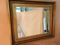 Frontal photograph of rectangular mirror with gold and bronze painted frame, showing reflections and frame condition.