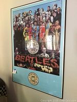 Full view of the framed poster hanging on a wall, showing the Beatles in colorful costumes and multiple cut-out characters and flowers spelling 'Beatles'.