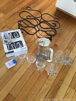 Photo showing metal wine rack with curved bottle slots, five double old fashioned glasses with card suit designs, French press coffee pot, and two framed wine prints stacked