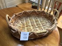 Full view of woven wooden basket on a wooden table, showing two handles and overall basket shape.