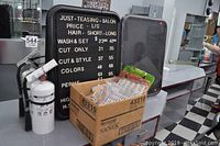 Photo of two letter price boards, one used with white letters and one new in packaging, next to a cardboard box of white push pin letters, 2 plexiglass sign easels, 2 clipboards, and a fire extinguisher in background.