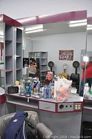 Full view of the hair dressing station including mirror, counter with drawers, shelves, and electrical outlets, showing items and various hair products on the counter and shelves.
