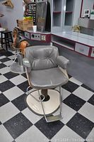 Full view of mid century modern hair dressing chair showing upholstery, armrests, base, and surrounding environment.