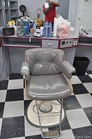 Photo of the hair dressing chair in front of a salon station showing the entire chair including backrest, seat, armrests, and base.