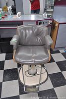 Front view of grey mid century modern hair dressing chair, showing cracked upholstery and laminate trim on seat edges, hydraulic base and footrest visible.