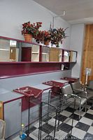 View of large hairdressing washing station with three sinks, three upper sliding mirrored cabinets, and base cupboards. Potted plants placed on top of cabinets. Unit installed against white wall over black and white checkered floor.
