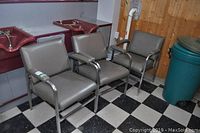 Three steel framed salon chairs with vinyl upholstery, armrests; placed in front of salon hair washbasins. Visible wear on chairs.