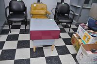 Small square laminate rolling table with maroon sides and a gray top, placed on checkered flooring in a room with chairs and boxes around.