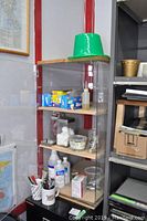 Acrylic locking cabinet with contents showing five removable shelves with items arranged inside, visible cracks and damage on door