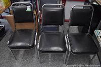 Three black vinyl vinyl chairs with metal tubular frames, seats 17x17 inches, height 34 inches, placed on grey floor with other items in background