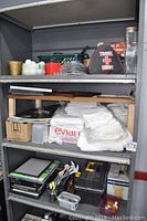 Three shelves filled with assorted household and hardware items, including a travel first aid kit, folded white towels, and black toolbox.