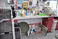 Wide photo showing barber station with countertop holding various items, on castors, with two red painted pedestals and a white plastic drawer unit beside one pedestal