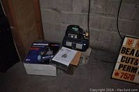 Air compressor on a wooden platform next to its box and manual in a basement or garage setting.