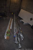 Two aluminum ladders side by side with pine and MDF trim pieces laid out on concrete floor.