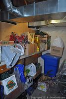 Long view showing shelves filled with about 15 boxes and bags containing Christmas lights, garlands, bulbs, star ornaments, and floral decorations stored and awaiting pickup.