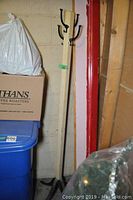 Coat rack standing in corner near wall; shows base and multiple hooks for hanging coats or hats.