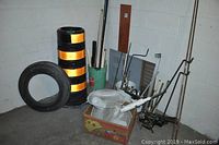 Photo of construction pylon, scrap metal rods, bucket with rods, tire, electric fan, and metal box in corner of basement room