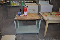 Metal cart with wood top, vice, and fire extinguisher shown in garage workspace with concrete walls and appliances in background.