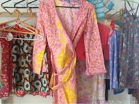 Handmade dresses and sweaters hanging on wooden racks with various colored hangers, showing floral and patterned designs.