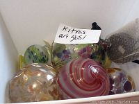 Six Kitras art glass pieces in a white box showing various colors and shapes including leaf accents and swirl patterns.