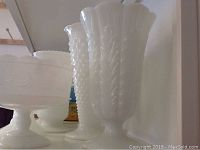 Multiple milk glass vases and compotes showing different textures and shapes including a hobnail vase and a tall ribbed vase.