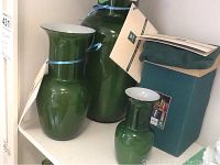 Front view of three olive green Murano glass vases with original box and COA visible.