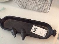Full view of the black cast iron bird feeder showing the long tray and one end's decorative ridge.